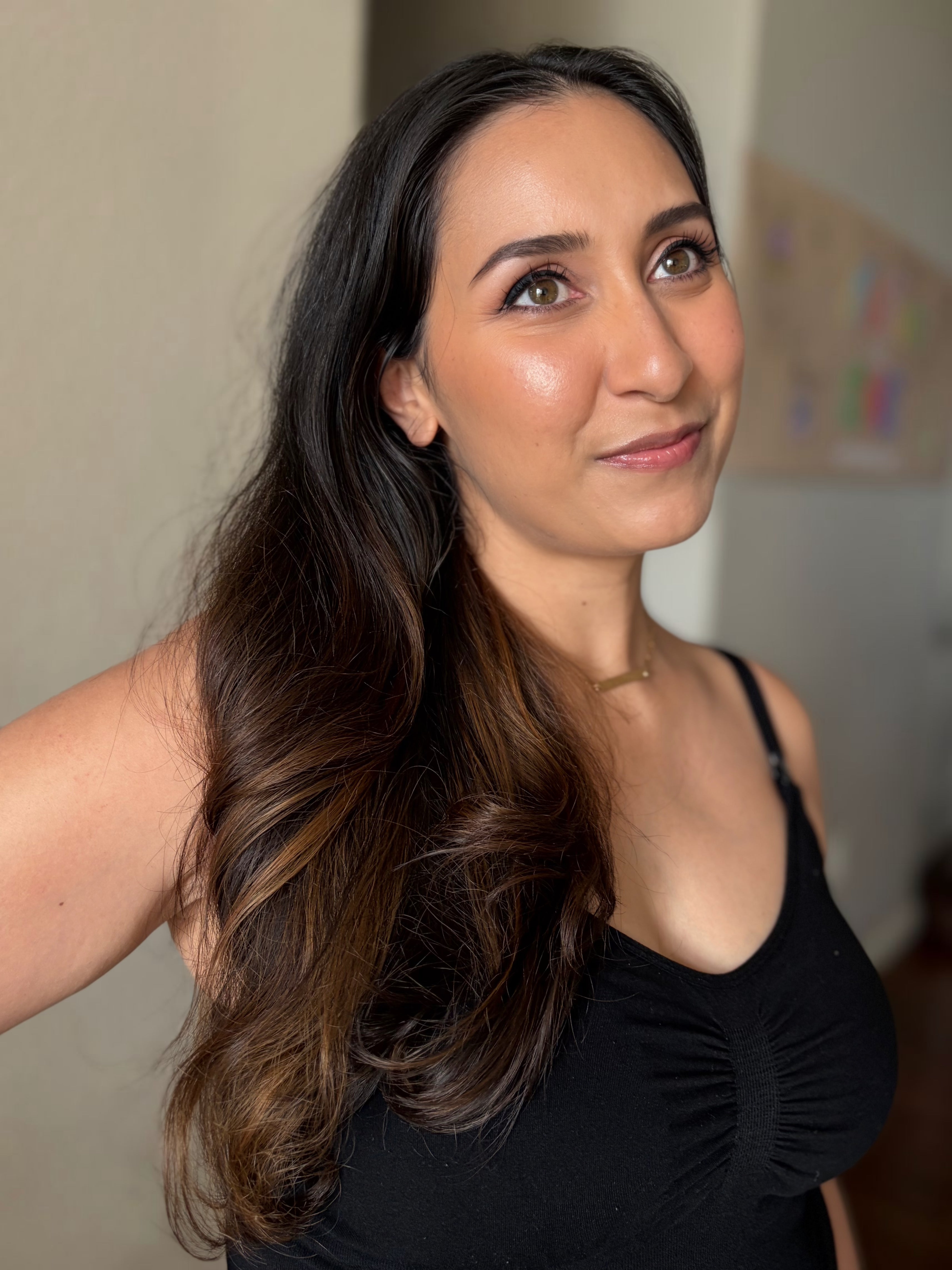 A woman with long, wavy dark brown hair wearing a black tank top, shown in a close-up portrait